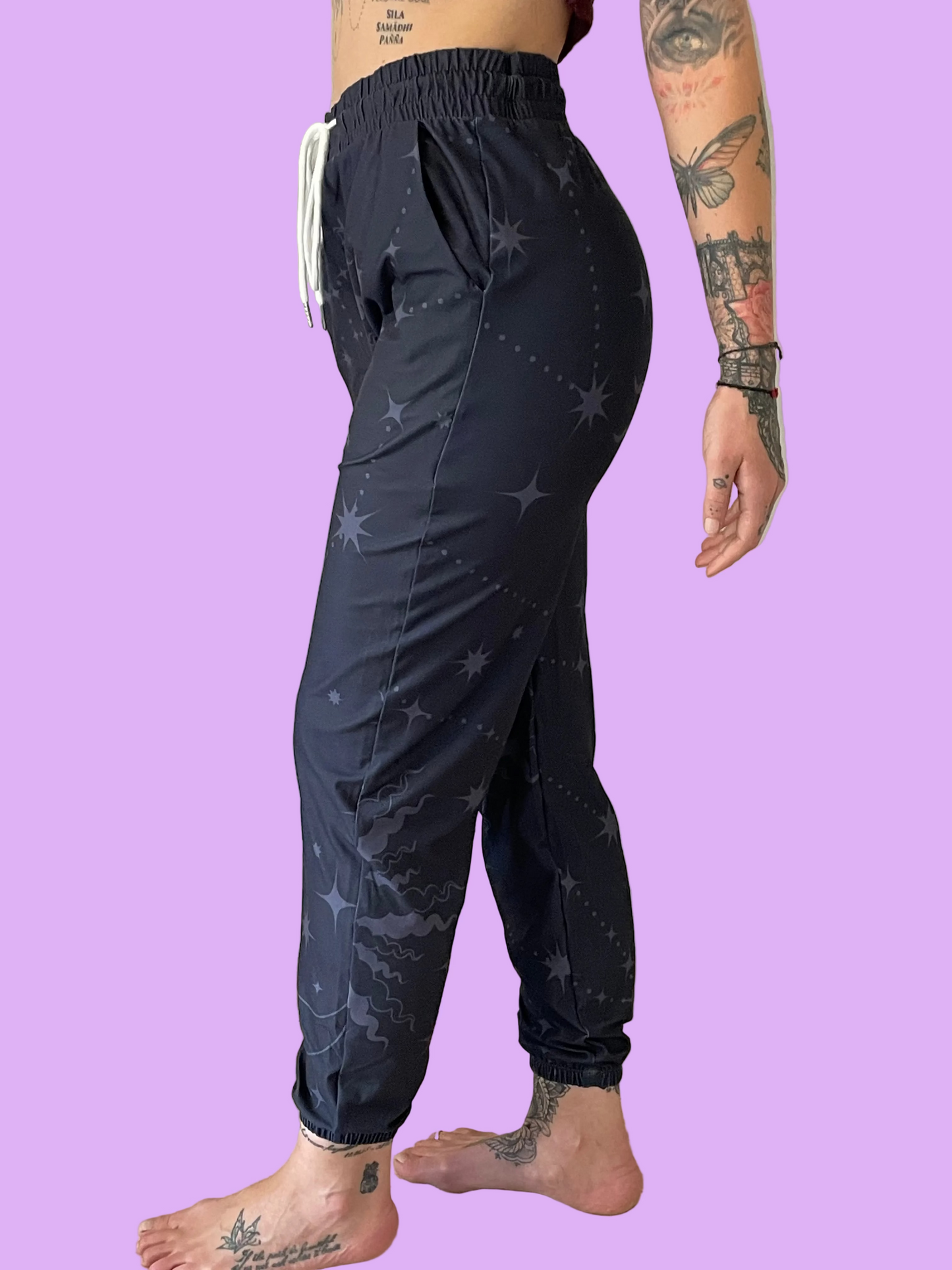 Person wearing black jogger pants with star pattern on a plain background